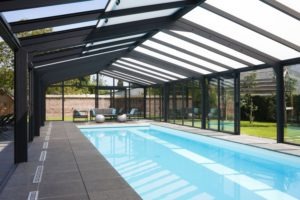 Véranda en aluminium gris foncé sur piscine intérieure bleue.